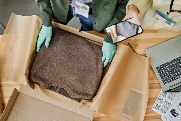 Top view of gloved hands of volunteer putting folded sweater into box