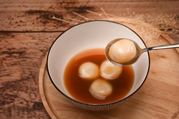 Top view glutinous rice balls with black sesame in sweet ginger soup on wooden table.