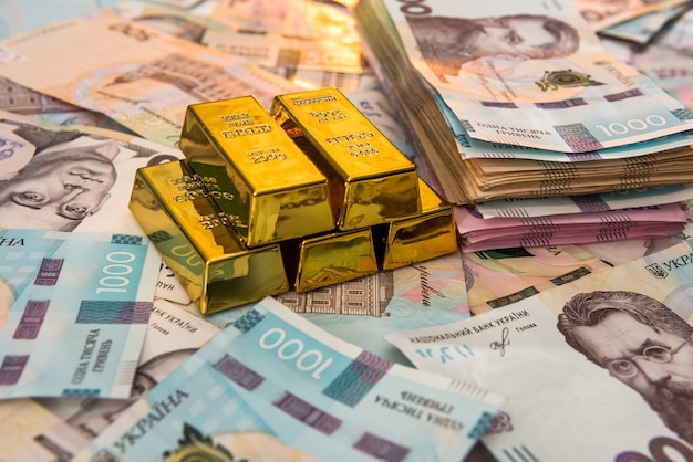 Top view of gold bars lying on a background of Ukrainian money. UAH. Save and money concept.  Financial background