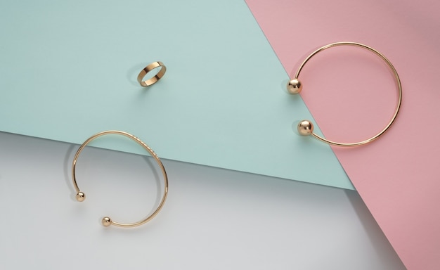 Top view of golden bracelets and ring on geometric pastel color background