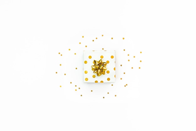 Photo top view of a golden dotted gift box and star shaped golden sequins on a white background.