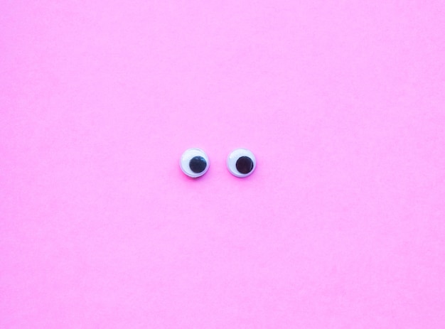 Top view of googly eyes on pink background with copy space.