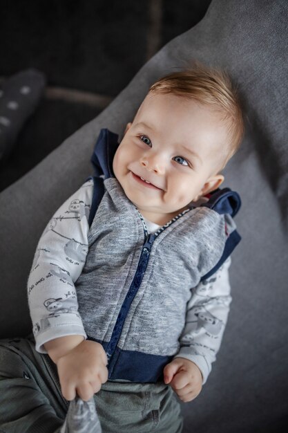 Top view of gorgeous caucasian toddler smiling, lying on couch and playing with his foot.