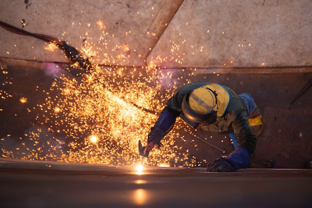 Vista dall'alto scriccatura saldatura scintilla fuoco saldatore industriale indossare maschera protettiva di sicurezza costruzione riparazione serbatoio olio saldatura per la parte in specifiche confinate