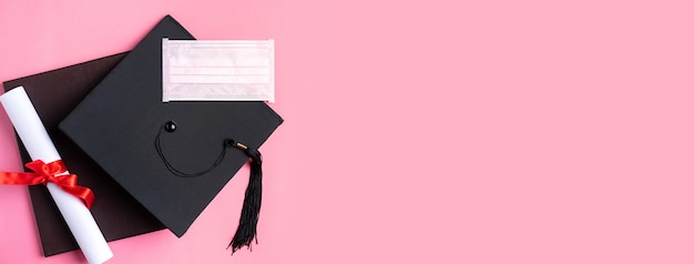 Photo top view of graduation square academic cap with degree diploma and mask isolated on pink table background.