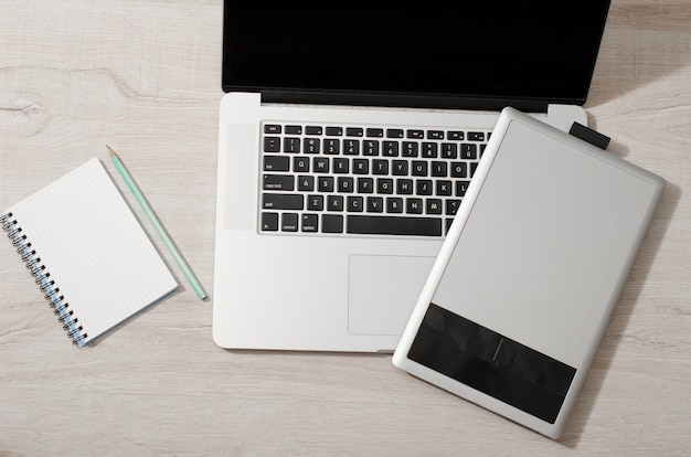 Top view of a graphics tablet, laptop keyboard, notebook and pencil