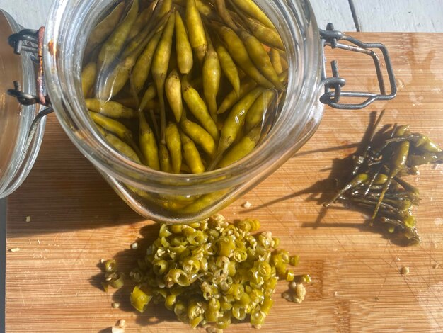 Photo top view of green chilies pickles on glass jar and cut pieces on chop board