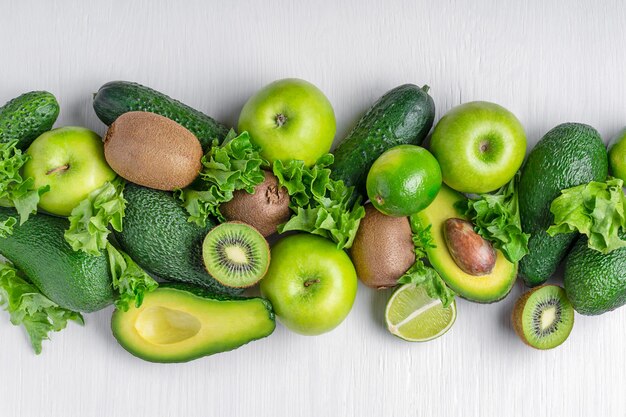 Top view of green fruits and vegetables used for healthy vegan dieting on white wooden background