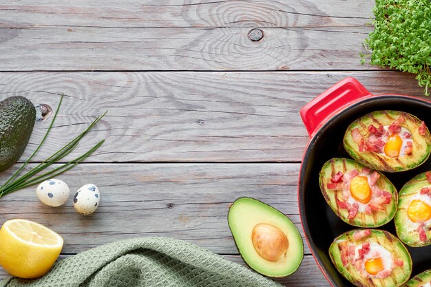 Top view on grilled avocado boats with bacon and egg, flat lay on wood