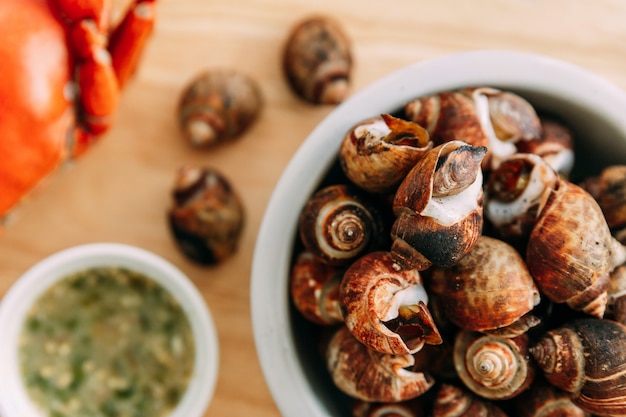 Photo top view of grilled laevistrombus canarium in shells served with thai spicy seafood sauce on wooden plate.