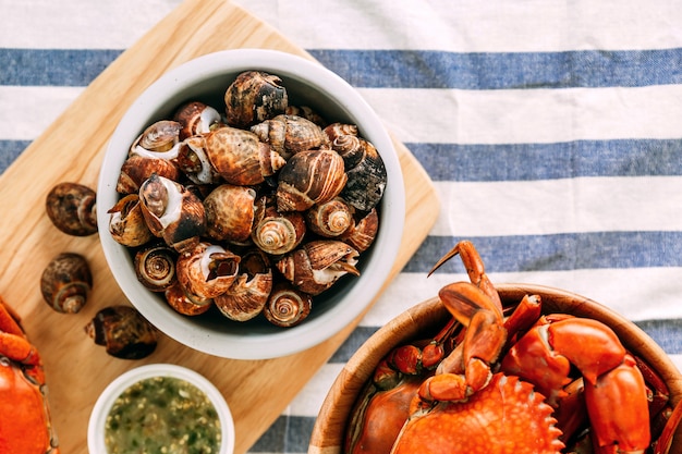 Photo top view of grilled laevistrombus canarium in shells with steamed giant mud crabs in wooden bowl.