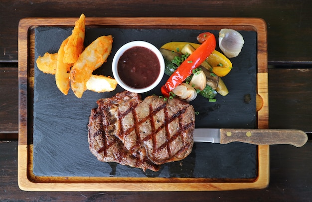 Top view of grilled ribeye steak with red wine sauce served on hot stone plate