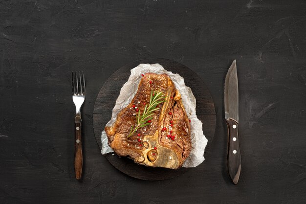 Top view of grilled t-bone steak with spices on black table