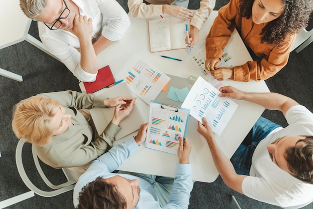 Top view group of serious businesspeople working together with graphs documents talking in office