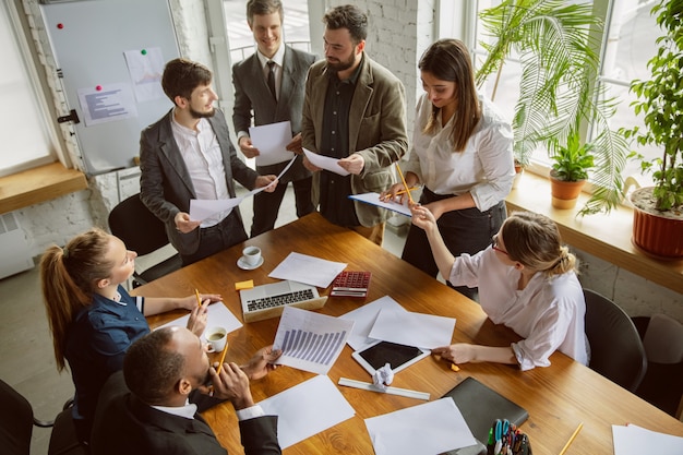 Top view. Group of young business professionals having a meeting. Diverse group of coworkers discuss new decisions, plans, results, strategy. Creativity, workplace, business, finance, teamwork.