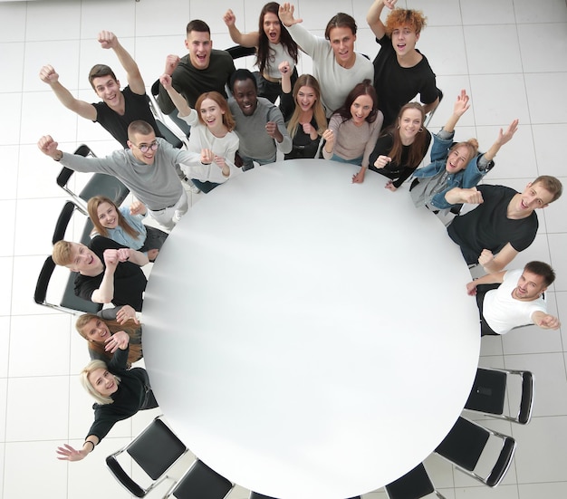 Top view group of young people standing near a large round\
table