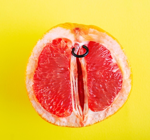 Photo top view half of grapefruit with piercing ring on yellow background