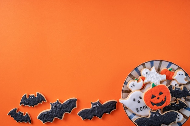 オレンジ色の背景にハロウィーンのお祭りの装飾が施されたアイシング シュガー クッキーの平面図