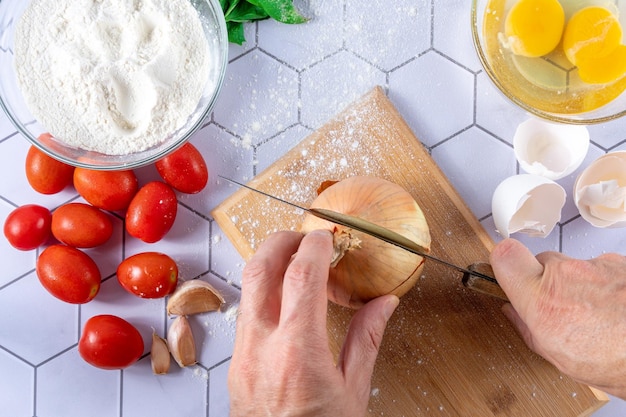 Top view of a hand cutting onion between ingredients and cooking instruments