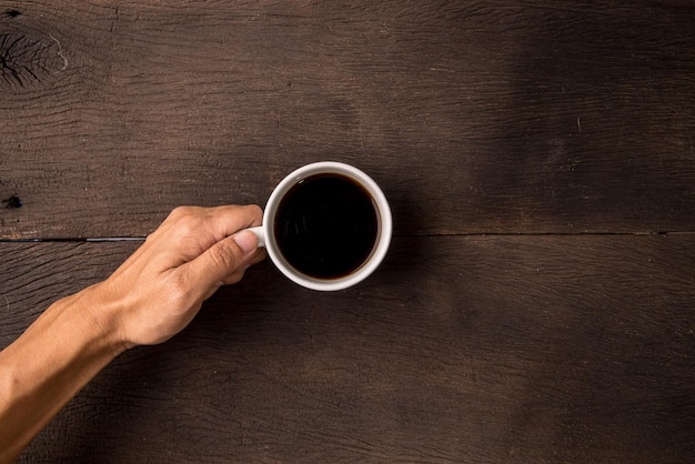 top view hand hold black hot coffee on wooden table