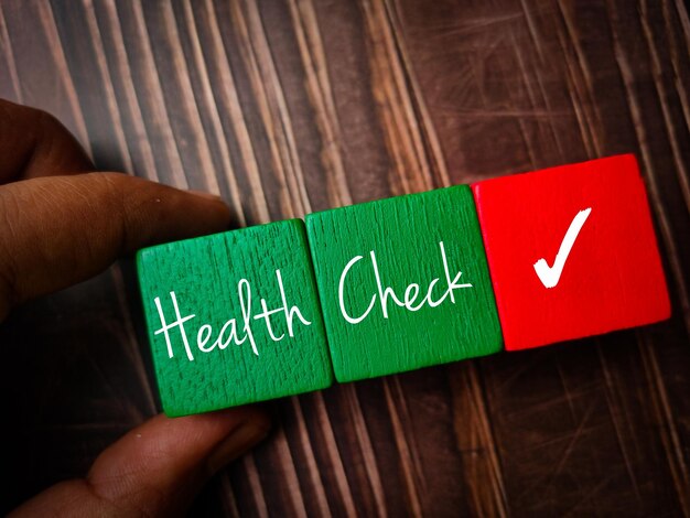 Foto vista dall'alto mano che tiene cubo di legno colorato con testo health check su uno sfondo di legno