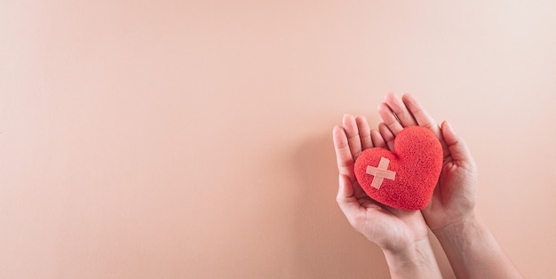 top view of hand holding red heart on pastel background