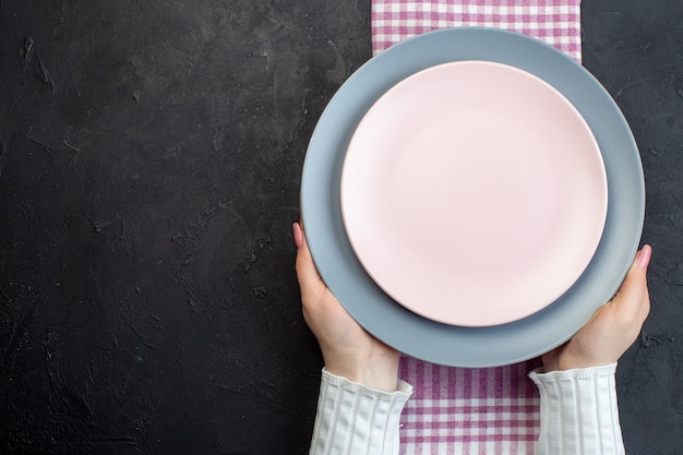 Top view of hand holding white and blue ceramic empty plates on folded pink stripped towel on black background with free space