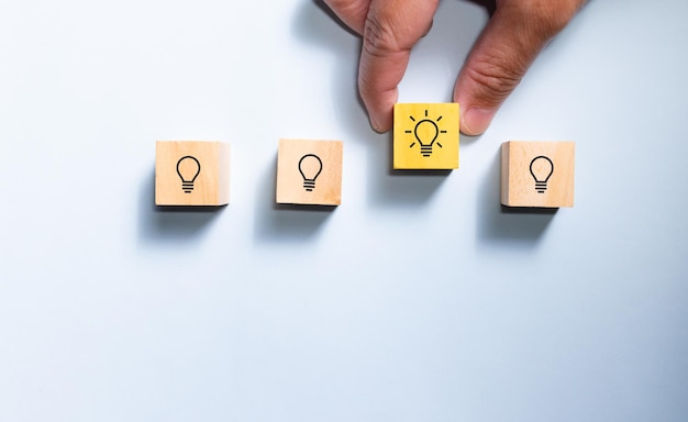 Top view hand pick wooden blocks with light bulb from the row\
concept for creative and design solution