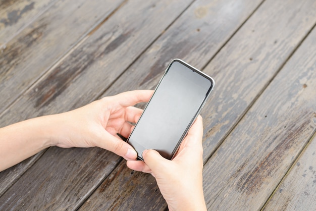 Top view hand using phone blank screen on the wooden table