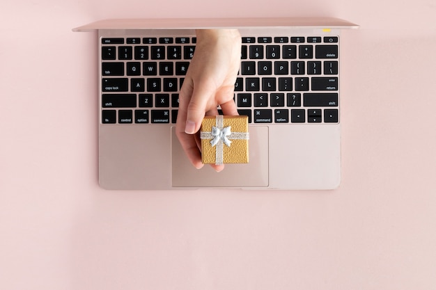 Top view of hand with a gift from laptop. Festive flat lay on pink background