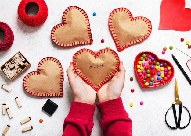 Vista dall'alto del cuore di carta fatto a mano con la parola mama stampata e riempita di dolci sulle mani dei bambini