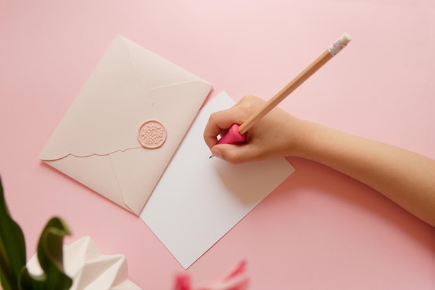 Top view of hands of anonymous child holding pink envelope with gift certificate