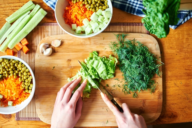 Top view of hands cutting lettuce on wooden board