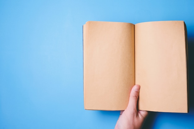 Top view of hands holding a blank book ready with copy space ready for text on blue background.