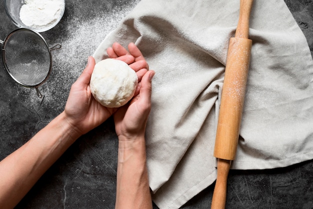 Top view hands holding dough near rolling pin