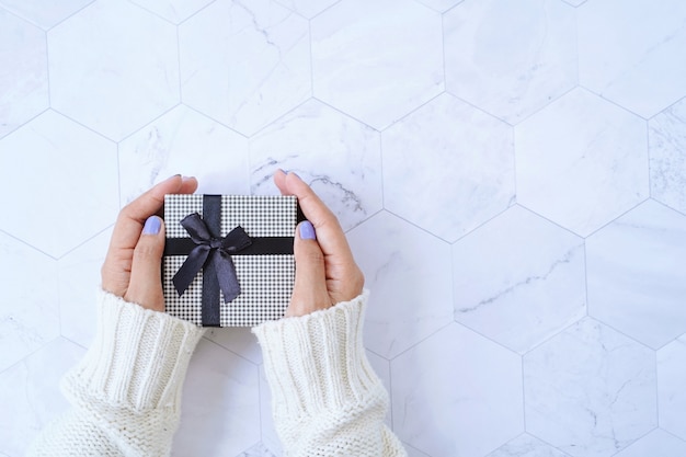 Top view of hands holding gift box from new year celebration or christmas present on white marble background, holiday concept