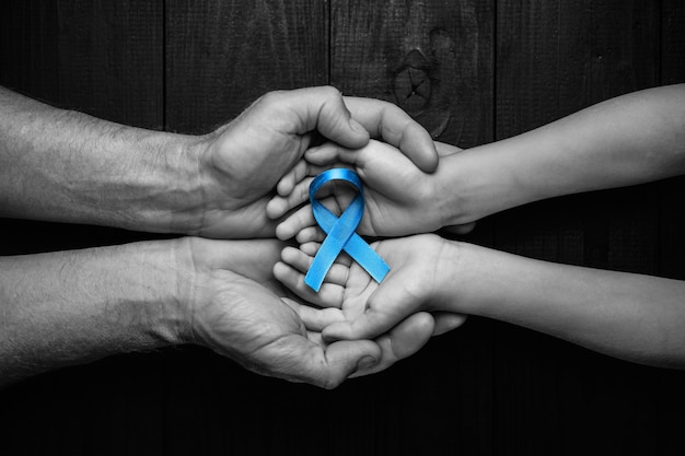 Top view on hands holding prostate cancer ribbon, colon cancer concept, blue ribbon symbol.black and white.