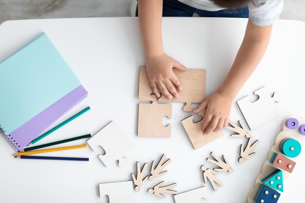 Foto mani di vista dall'alto del bambino che organizza puzzle in legno simbolo della consapevolezza pubblica per l'autismo
