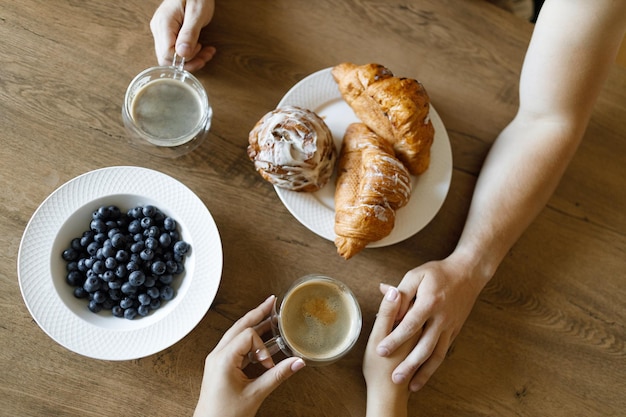 Photo top view of hands of man and woman enjoying coffee croissants and blueberries