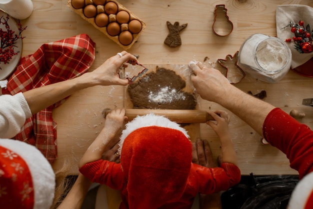 Photo a top view of the hands of mather father and child in a santa hat rolling dough with a rock