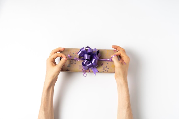 a top view hands tighten a bow pf a color ribbon on present box on white table