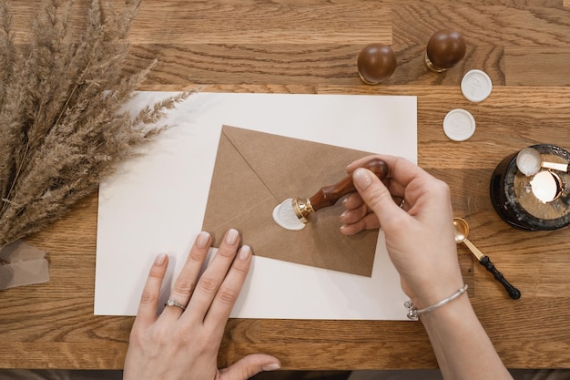 Top view of hands of unrecognizable woman making white wax seal\
with stamp on brown greeting envelop