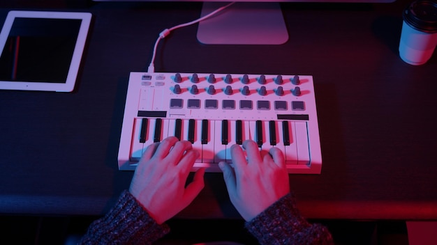 Top view of hands using midi keyboard in home studio with neon\
lights