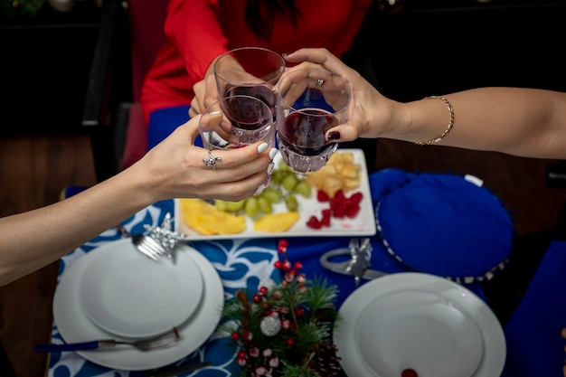 Vista dall'alto delle mani con gli occhiali che brindano a una cena di natale con decorazioni natalizie sul retro