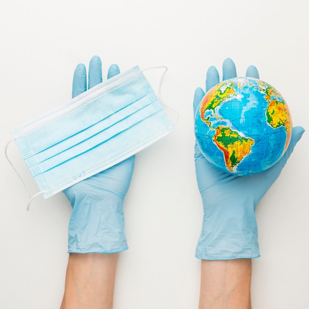 Top view of hands with gloves holding earth globe and medical mask