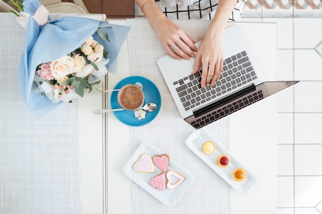 Top view of hands of young woman using laptop ath the table in cafe