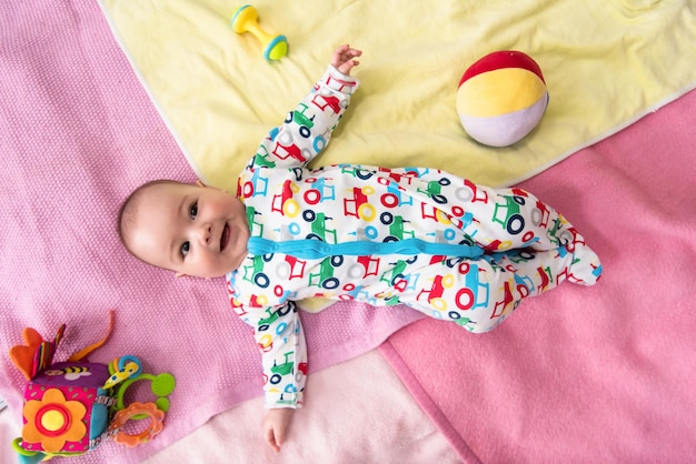 top view of happy beautiful newborn baby boy lying on colorful blankets while playing first games at home