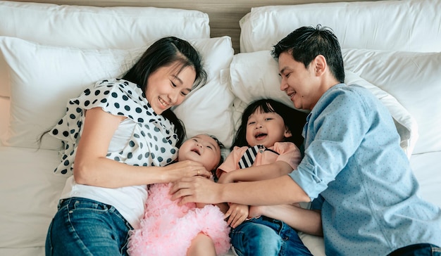 Vista dall'alto della famiglia felice si diverte in camera da letto godendo di stare insieme i genitori stanno solleticando il loro bambino mentre sono sdraiati a lettoattività di fine settimana concetto di stile di vita familiare felice