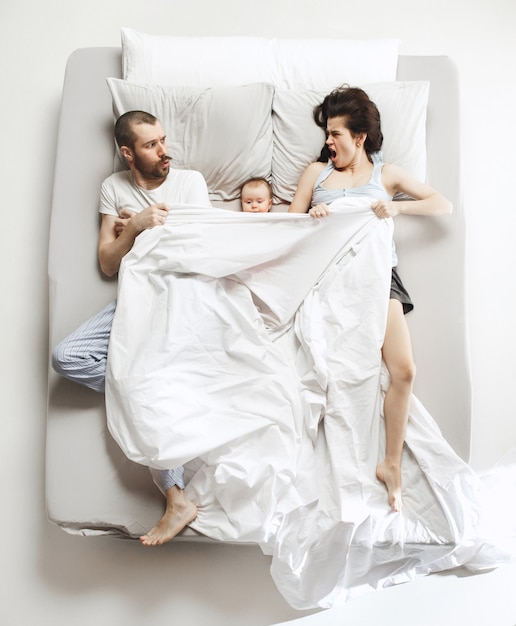 Top view of happy funny family with one newborn child in bedroom. Enjoying being together. Happy family in bed. Top view. Emotions concept. Morning after sleep. Family lifestyle. happy parents concept