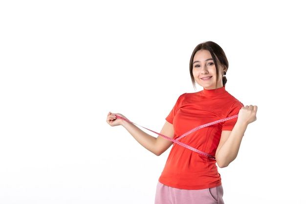 Top view of a happy smiling young lady gathering her hair dressed in redorange blouse and holding metre measuring her waist on white background